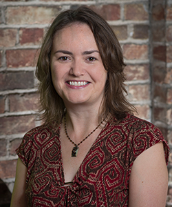 woman with shoulder-length brown hair wearing a red geometric print blouse and a pendant necklace